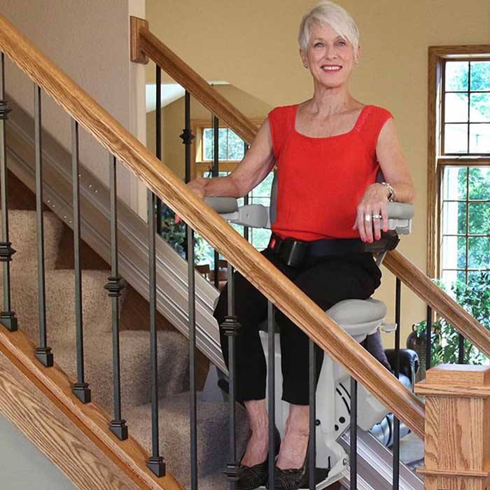 Elderly Woman Sitting on a Stair Lift Going Upstairs a Staircase in Williamstown, NJ